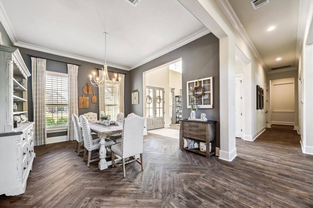 The formal dining room is perfect for entertaining, with ample space for your banquet table and sideboard. Wood-look tile flooring in a striking herringbone pattern is highlighted by thick crown molding, designer paint, and a stylish chandelier. Tall windows with wood shutters invite soft natural light, creating a warm and welcoming setting for unforgettable gatherings.