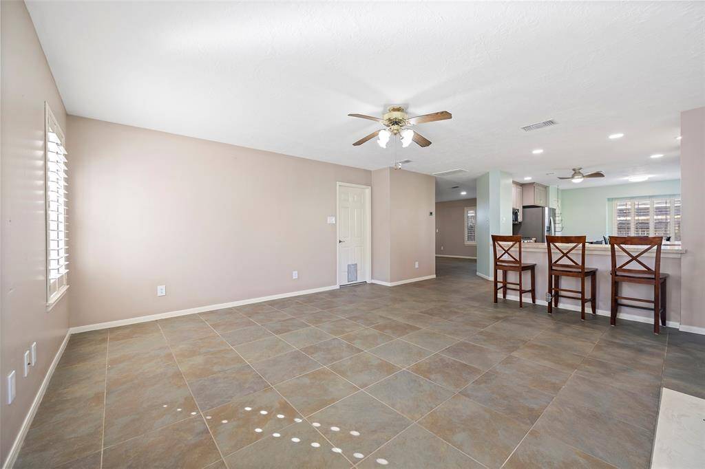 This spacious, open-concept living area features elegant tile flooring and ample natural light. The kitchen boasts a convenient breakfast bar with seating, perfect for casual dining and entertaining.