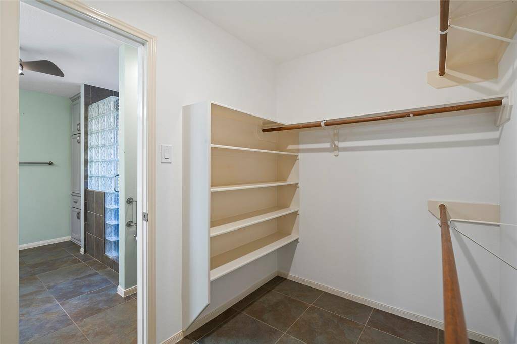 Discover a spacious walk-in closet featuring ample shelving and hanging space, seamlessly connected to a beautifully tiled bathroom for ultimate convenience.