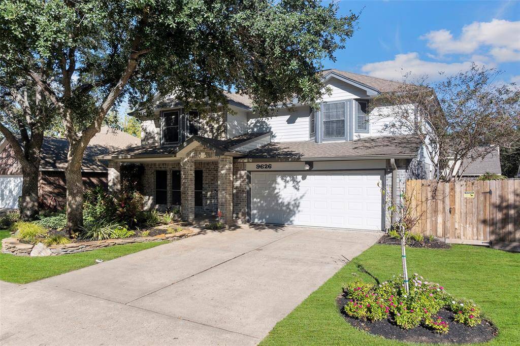 Charming two-story home with a brick and siding exterior, featuring a two-car garage. The well-maintained front yard includes mature trees and landscaped flower beds, offering excellent curb appeal.