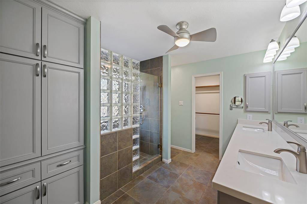 Your primary bath is spacious, modern bathroom featuring sleek double sinks, ample storage, and a stylish walk-in shower with glass block accents. Perfect for luxury and convenience.
