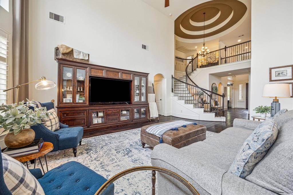 This striking view from the family room showcases the show-stopping rotunda ceiling and sweeping staircase, creating a truly dramatic statement. The open layout, with rich hardwood flooring and elegant wrought-iron railings, seamlessly connects the family room to the rest of the home, perfect for both grand entertaining and everyday comfort.