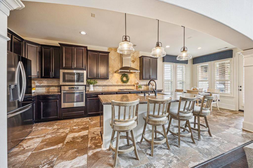 This chef-inspired kitchen is both beautiful and functional, featuring granite countertops, tile backsplash, sleek stainless steel appliances, and a large center island with bar seating and chic pendant lighting above.