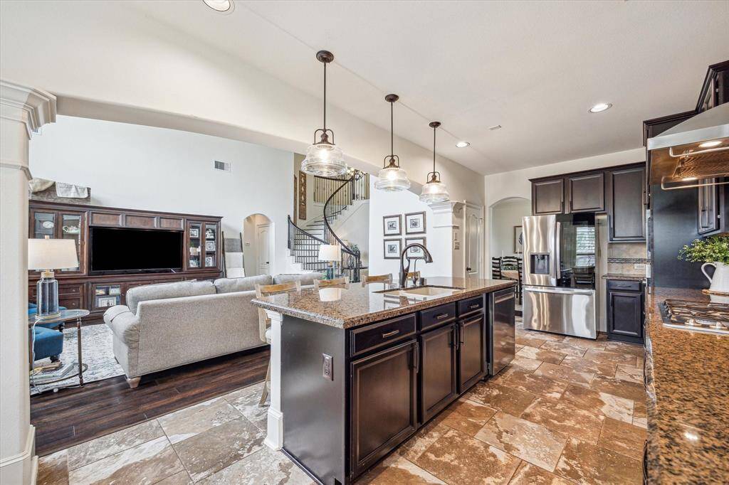 This view highlights the kitchen’s open-concept design, with clear sightlines into the family room and beyond. An expansive island topped with stylish pendant lighting creates a natural gathering place, combining elegance and practicality in a space tailored for today’s modern lifestyle.