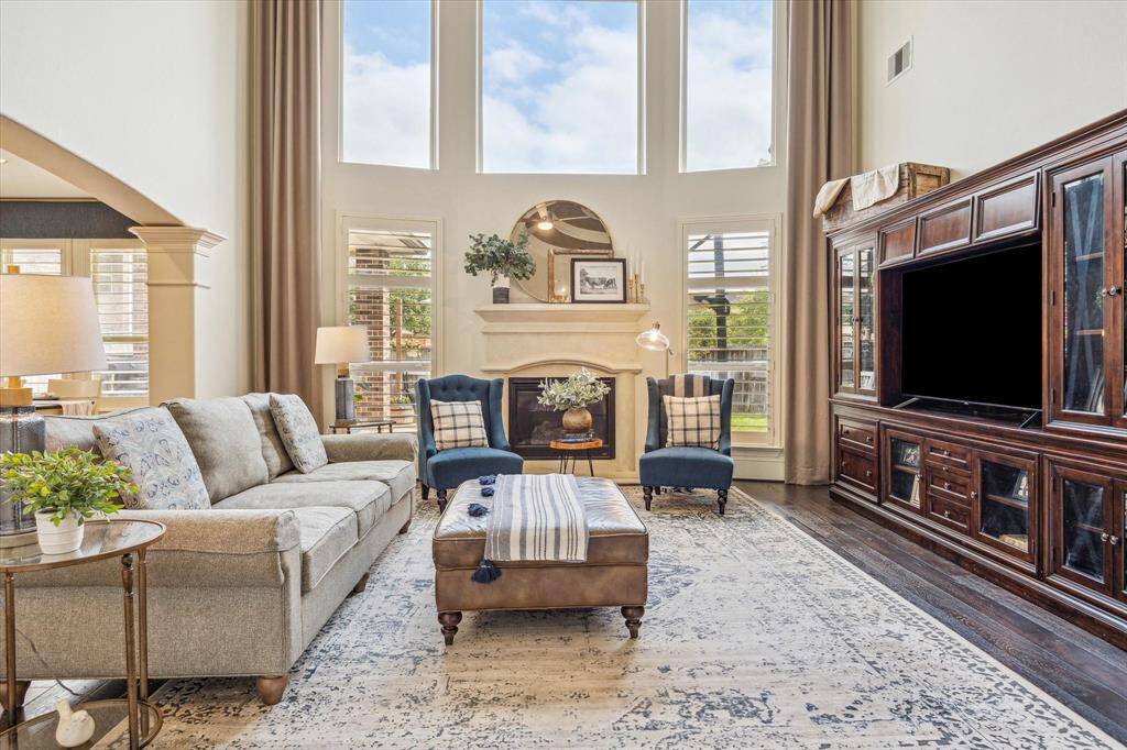 This elegant family room showcases rich hardwood flooring and a dramatic wall of stacked windows that floods the space with natural light. At its heart, a romantic gas-log fireplace anchors the room, creating a cozy and inviting setting for both relaxed living and refined entertaining.