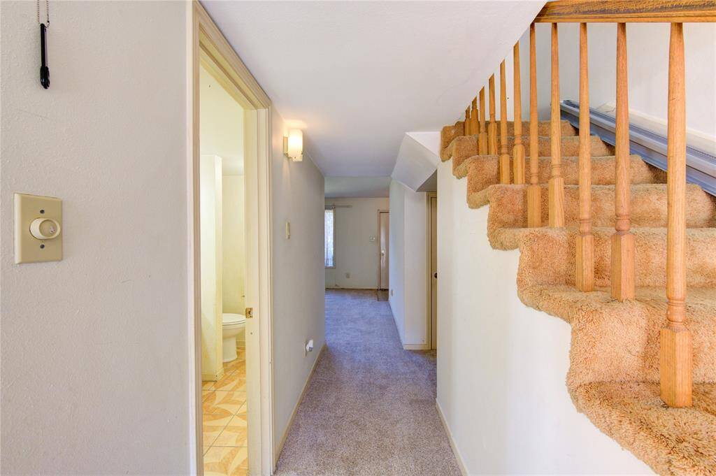This photo shows a hallway with carpeted stairs leading to an upper level. The space features neutral walls and access to a bathroom with on the left.