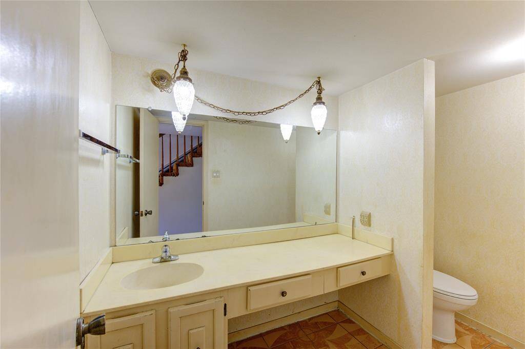 This photo shows a vintage style bathroom with a large mirror, a single sink vanity and hanging light fixtures