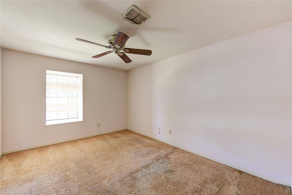 A bright, spacious room with a large window letting in natural light. It features neutral walls, a ceiling fan, and carpeted flooring.