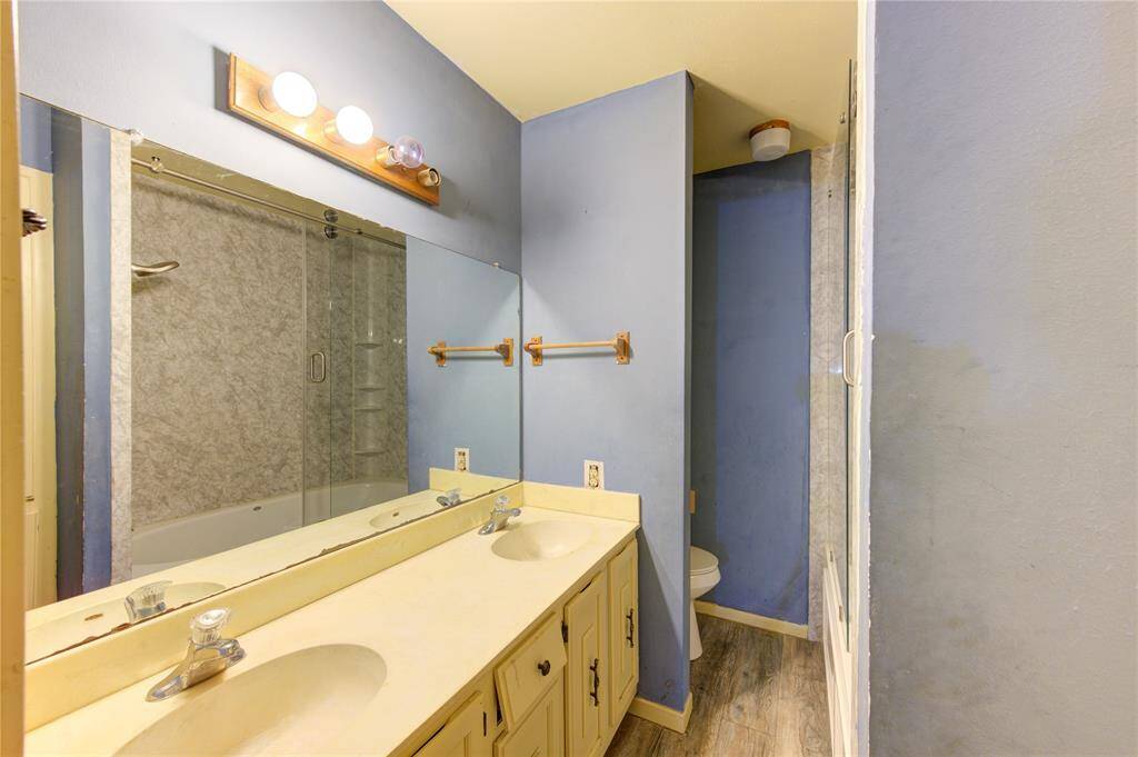 This bathroom features a bathtub with a glass sliding door and a marble patterned surround. There is a double vanity with light-colored countertop.