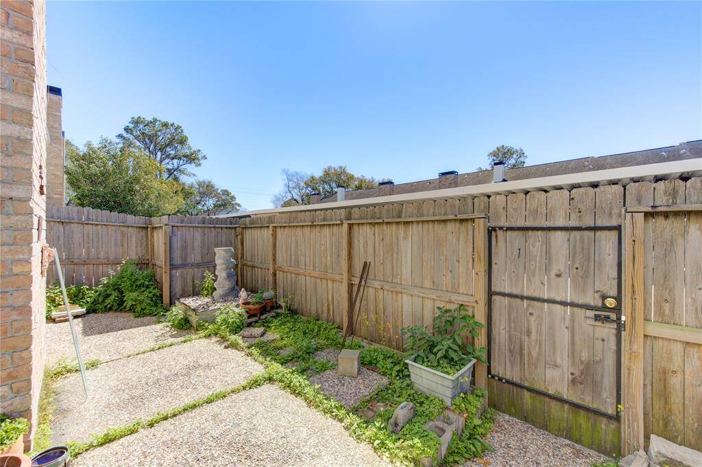 This photo shows an inviting fenced backyard with a wooden privacy fence and adorned by potted plants. The area is sunny and has potential for a cozy garden and outdoor seating