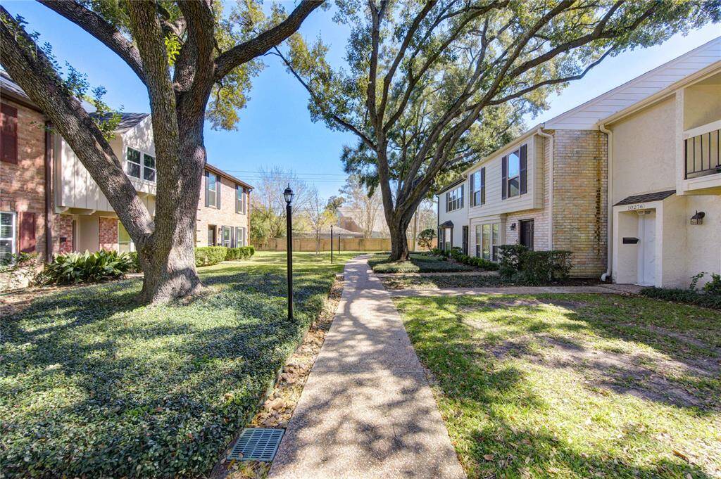 A view of the charming residential area with a well maintained walkway lined by mature trees. The houses are two-story, brick and siding structures, offering a cozy neighborhood feel.
