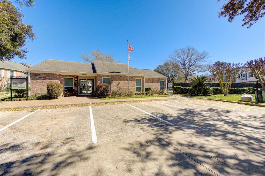 a photo of the community club house featuring a single-story brick building with a gabled roof, surrounded by well maintained landscaping. The setting is sunny and open, suggesting a welcoming community space