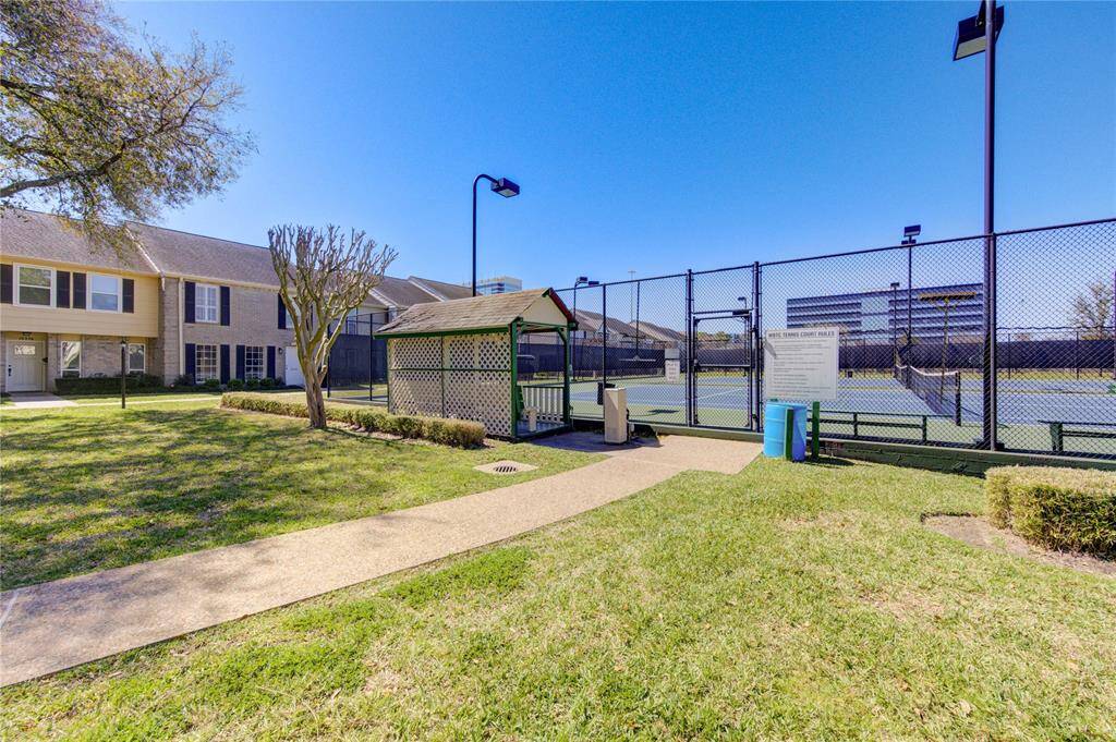 The well maintained community tennis courts surrounded by a pathway and landscaped greenery, offering a recreational amenity within a residential area.