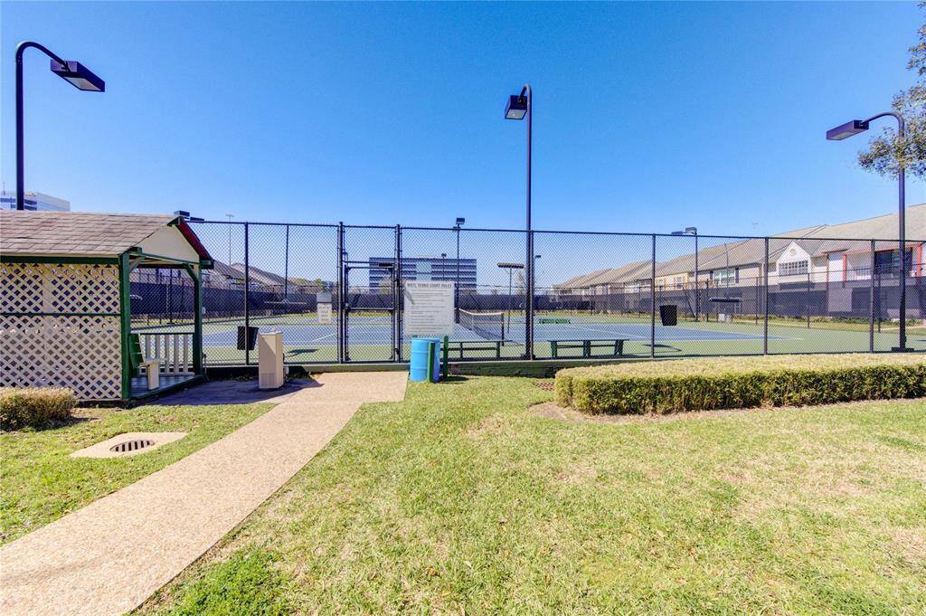 Tennis courts within the community, surrounded by a secure fence and landscaped greenery, with nearby amenities such as benches and s small pavilion.