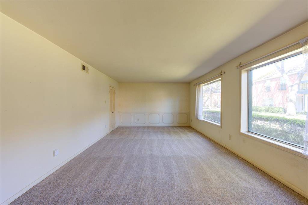 Spacious living room with neutral walls and carpet, featuring large windows that offer plenty of natural light and great views of the outdoors.