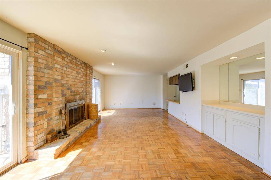 Spacious living area with parquet flooring, neutral walls, ample natural light. Features an open staircase with carpeted steps, built in cabinetry and a wall mounted TV. Ideal for entertaining and family gatherings.