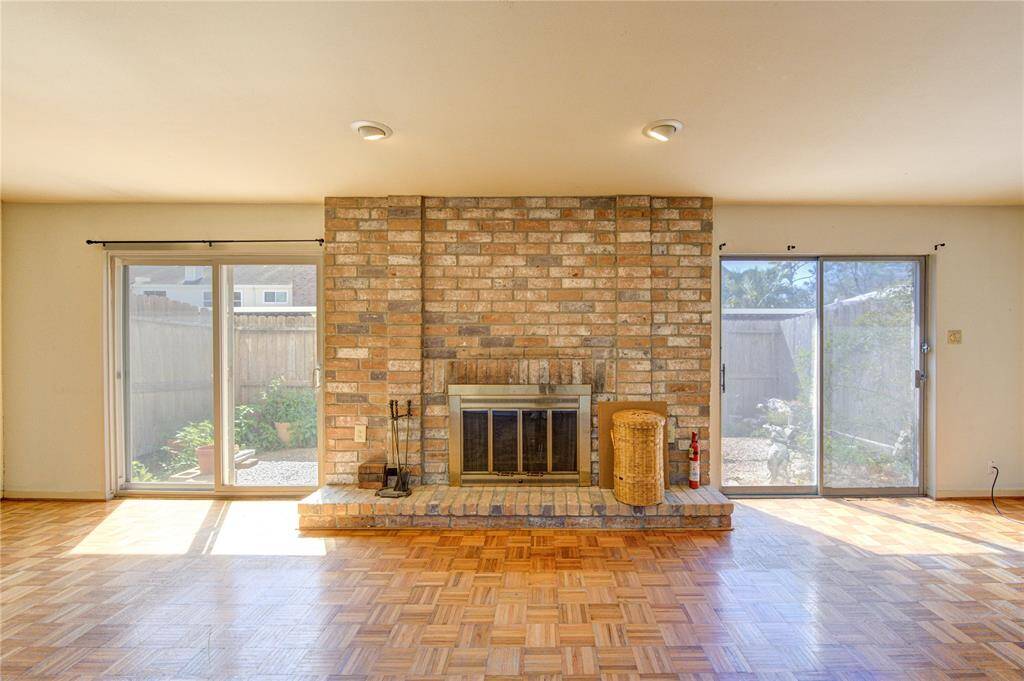 This spacious living room features a warm brick fireplace, parquet wood flooring, and ample natural light from large sliding glass doors.