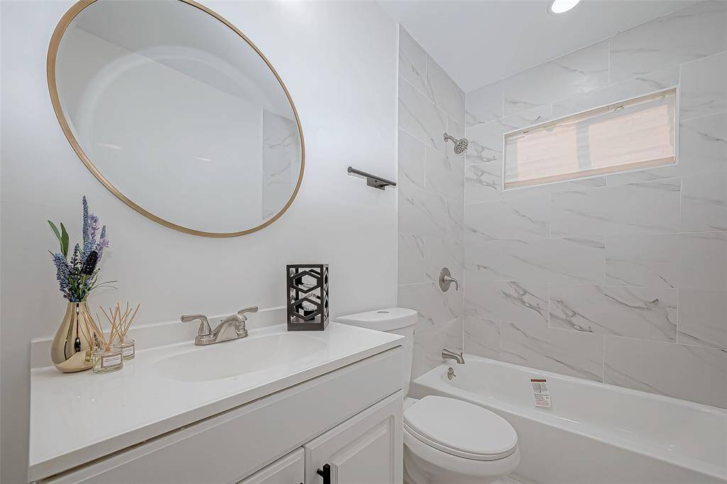 The secondary bathroom is both functional and stylish, featuring a classic shower-tub combo. The space is enhanced by clean, white tiles offering a timeless appeal while providing the perfect environment for everyday use.