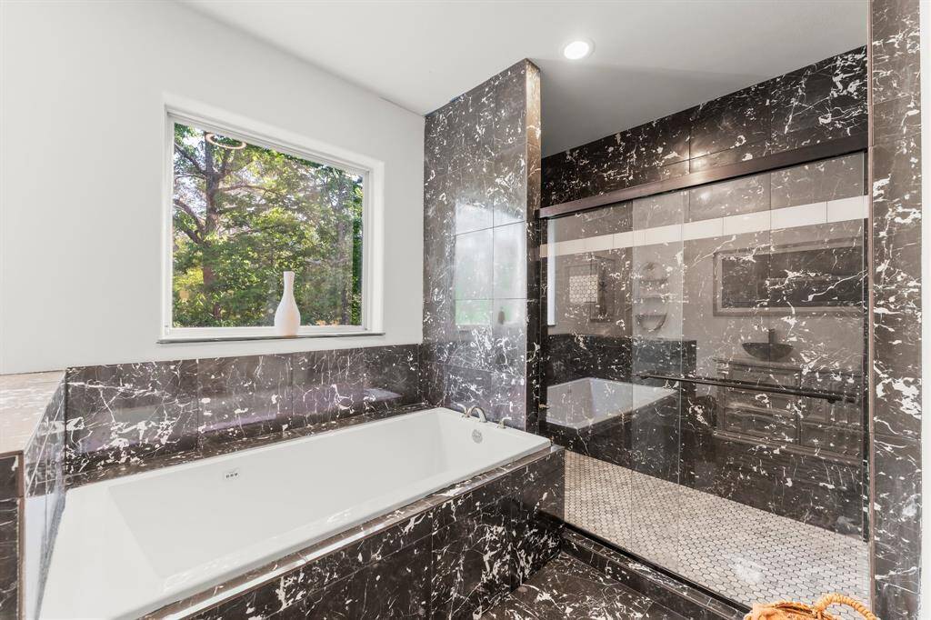 Elegant bathroom with a separate soaking tub and a modern, enclosed shower. Features stylish tile work and natural light.