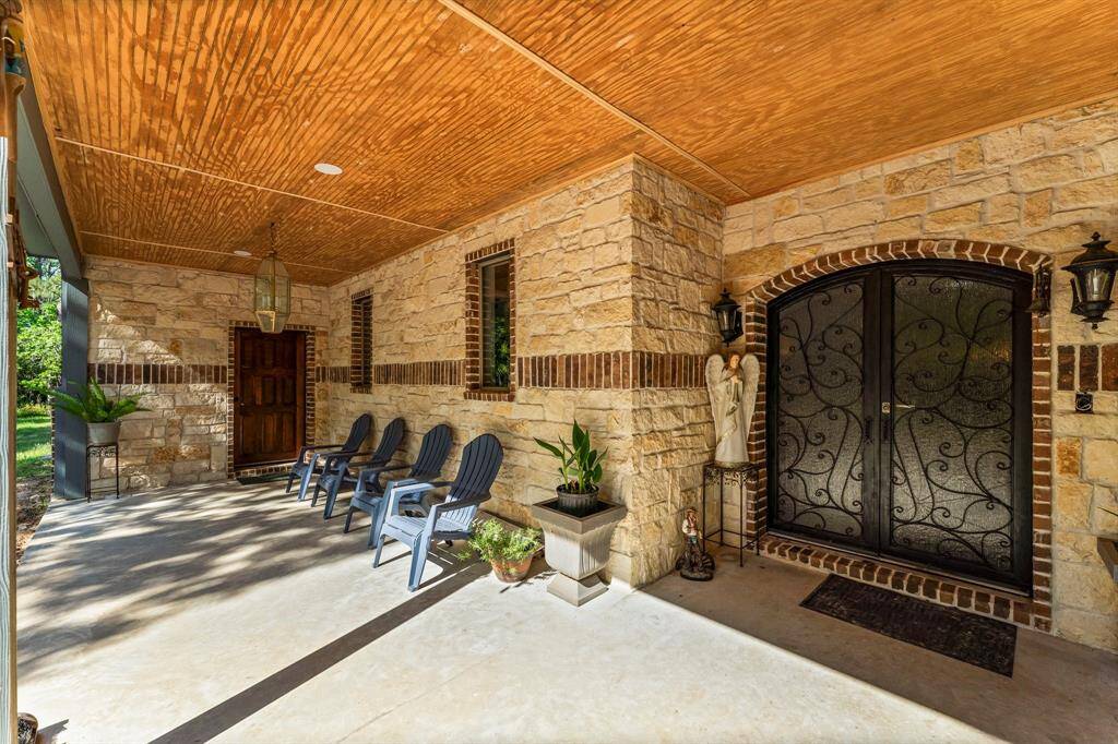 Admire the charming architectural details of this home, including the stunning stone walls and the signature iron grillework on the double front doors. The spacious covered porch provides a shaded retreat, enhanced by thoughtful lighting and creating a warm and inviting ambiance.