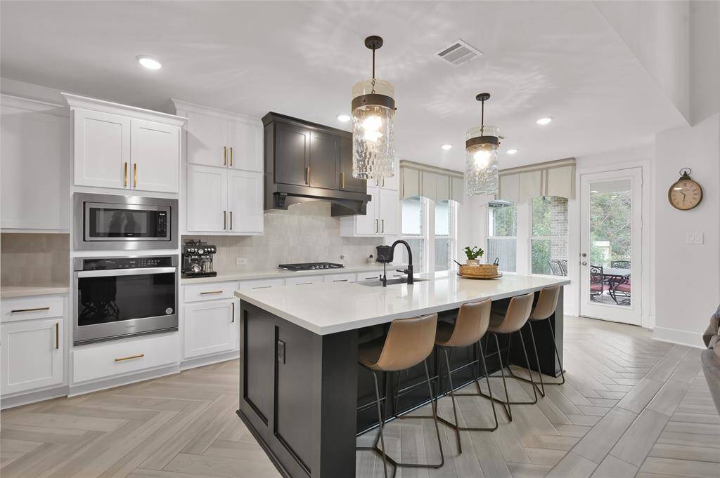 This kitchen features after market upgrades such as new pendant lights, additional trim work and paint to the island, custom vent hood, and window coverings.  This is in addition to the builder upgrades such as the 5-burner cooktop, built in appliances, and single-basin sink!