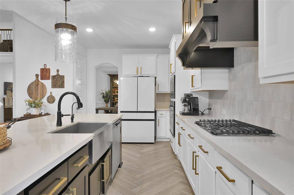 This kitchen features after market upgrades such as new pendant lights, additional trim work and paint to the island, custom vent hood, and window coverings.  This is in addition to the builder upgrades such as the 5-burner cooktop, built in appliances, and single-basin sink!