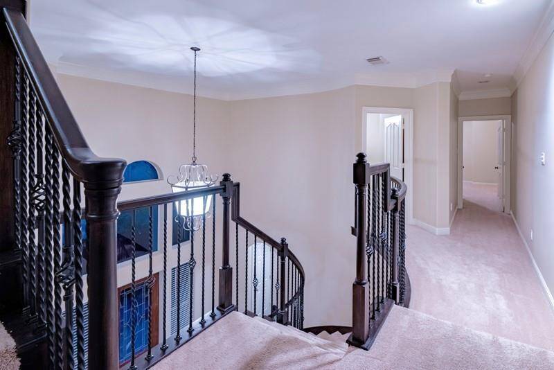Bright, carpeted upstairs landing with elegant dark wood and iron railing.
