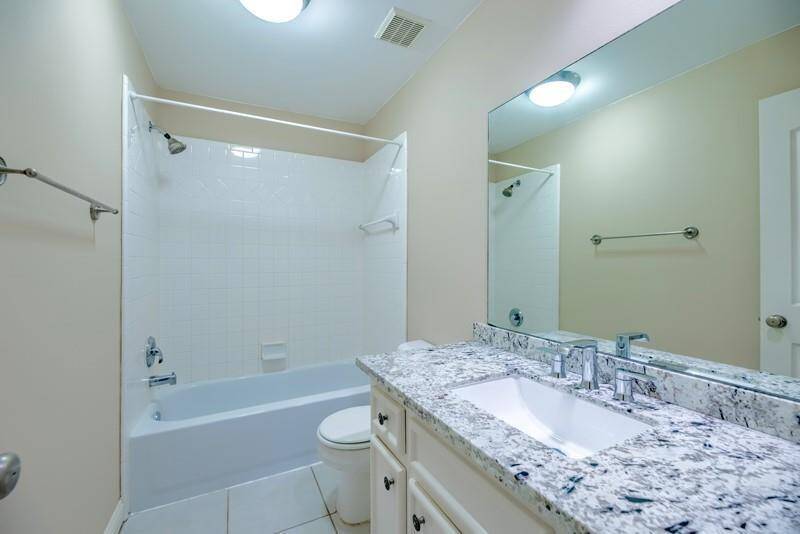 This bathroom features a sleek design with a granite countertop, under-mount sink, and a large mirror. It has a bathtub with a shower, white tiled walls, and neutral-colored walls and flooring, creating a clean and modern look.