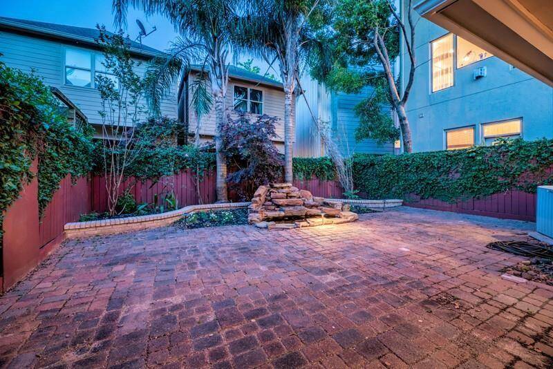Backyard boasts a generous brick patio surrounded by lush greenery and a charming rock fountain.
