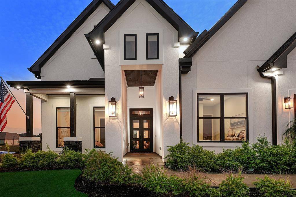 Stunning stucco elevation with black trim and front porch surrounded in tasteful landscaping.