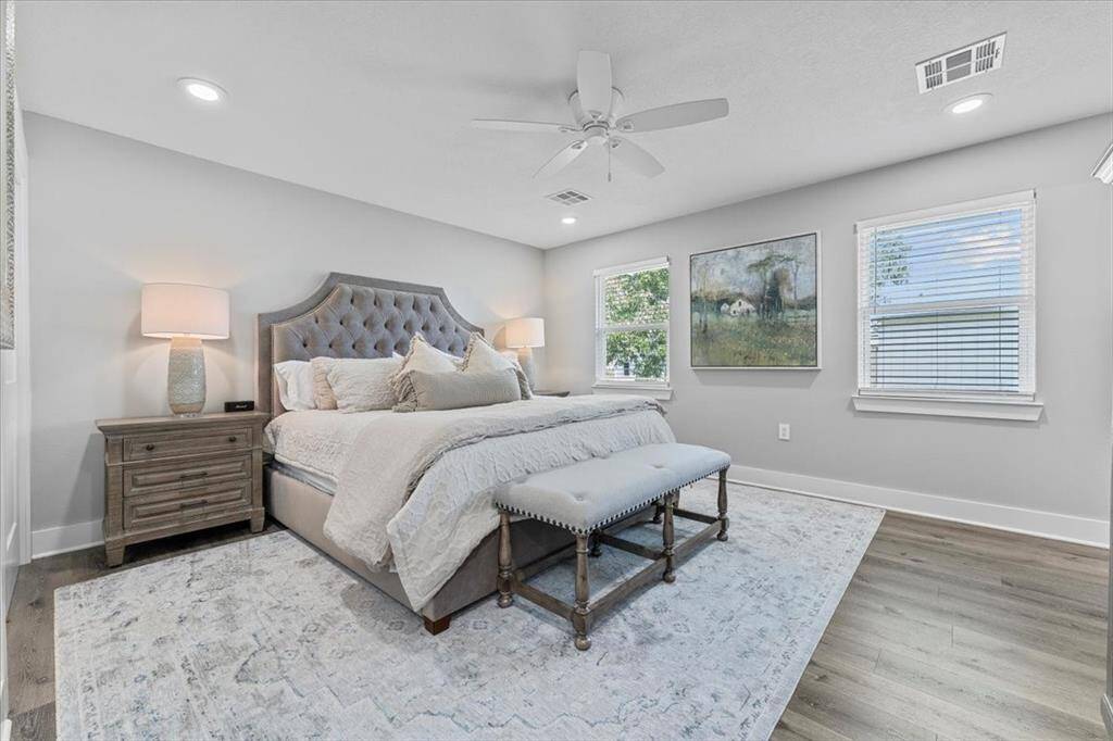 This is a bright and spacious bedroom with neutral decor, and large windows. It features a ceiling fan, a large walk-in closet.