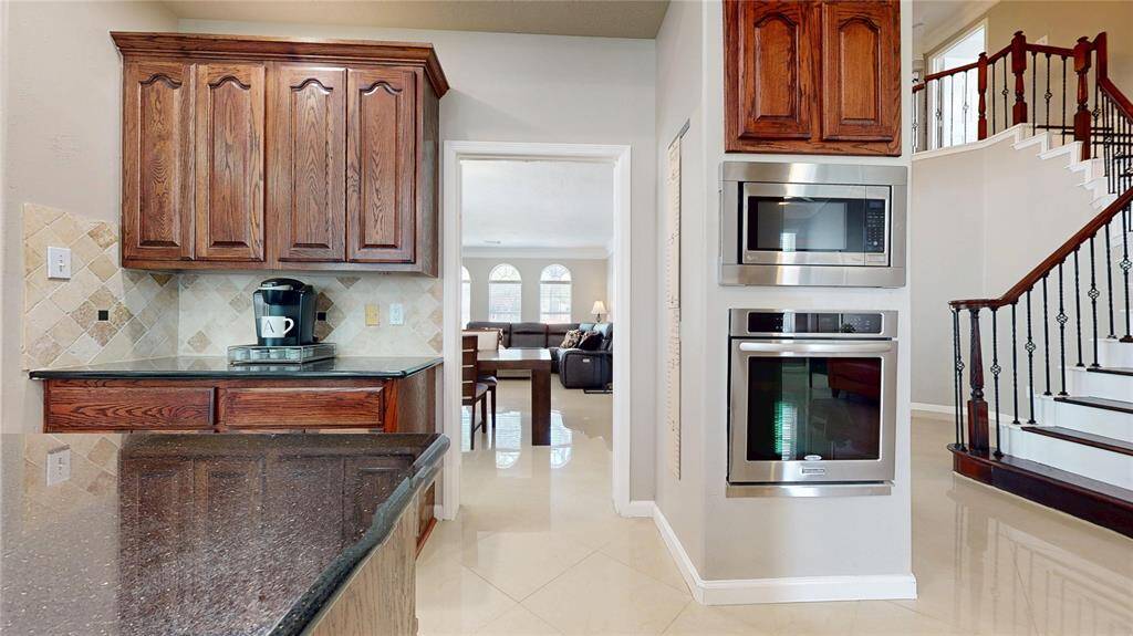 This photo showcases a modern kitchen with wooden cabinetry and stainless steel appliances. A view of a staircase featuring elegant railings leads to the second floor.