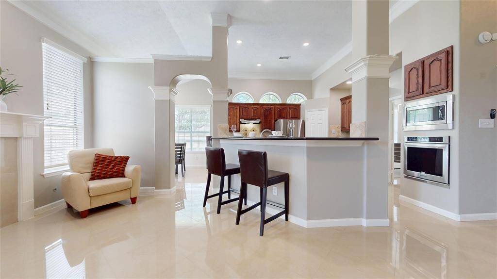 This spacious kitchen features a sleek breakfast bar with seating, modern appliances, and elegant cabinetry. The open layout flows into a bright living area with large windows and polished floors, creating a welcoming atmosphere.