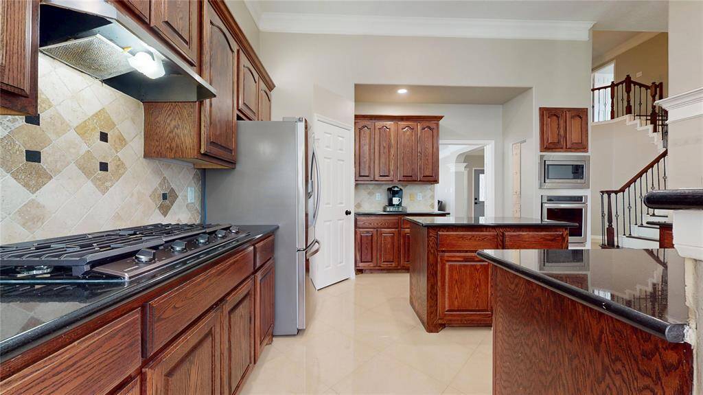 This kitchen features rich wood cabinetry, granite countertops, and a tile backsplash. It includes stainless steel appliances, a spacious island, and a gas cooktop, providing a functional and elegant cooking space.
