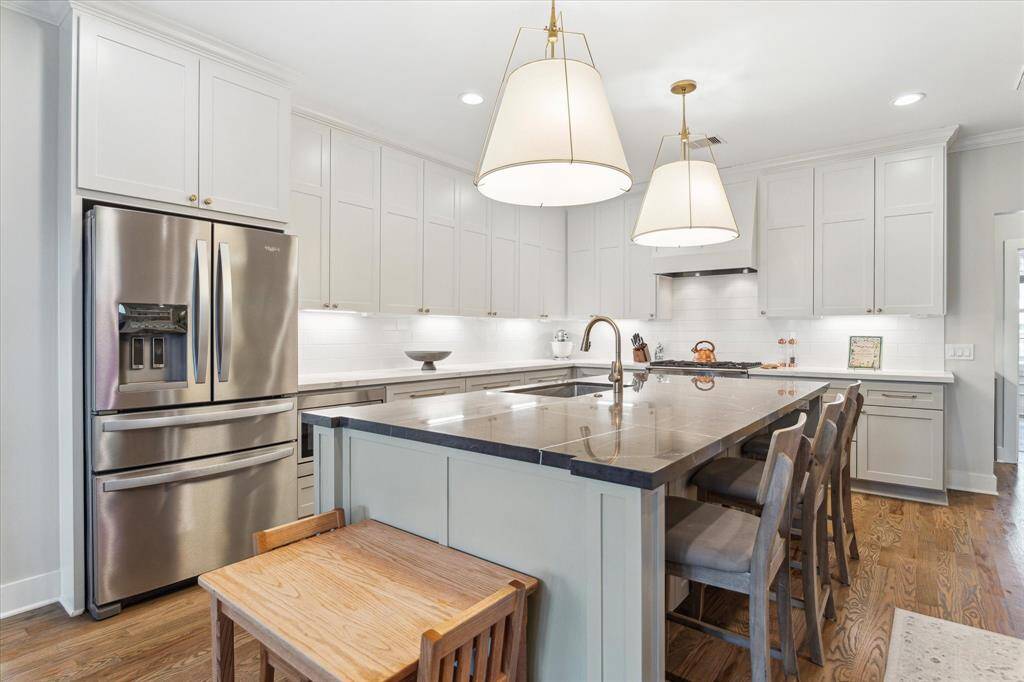 Brass hardware and fixtures add a modern touch, while oversized pendant lights provide ambient task lighting over the island. A stainless Whirlpool French door refrigerator, gas range with vent hood, and built-in microwave ensure the space is fully equipped for everyday cooking and entertaining. Tucked just under the island is a charming custom nook with a small-scale table, perfect for young children to join in on kitchen conversations or snack time.