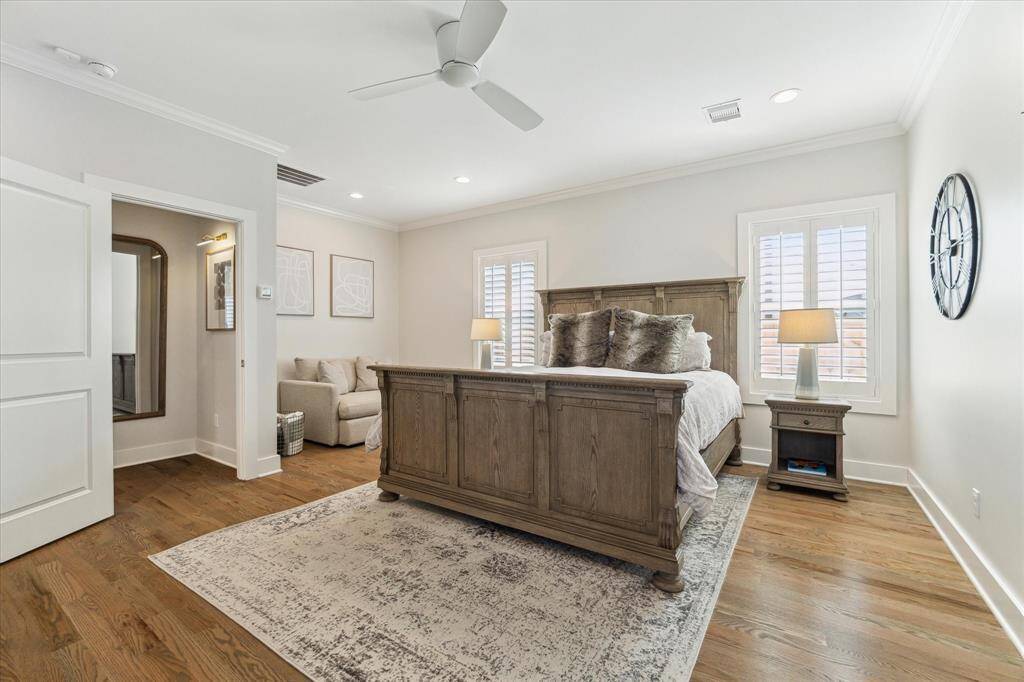 Rich hardwood floors and soft neutral tones bring warmth to this serene primary bedroom. Plantation shutters filter in natural light, while recessed lighting and a ceiling fan add comfort and functionality. A cozy sitting area near the entrance provides a quiet nook for reading or unwinding.