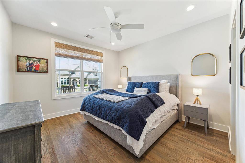 Large windows fill this secondary bedroom with natural light, while warm wood floors and soft wall tones create a relaxed, airy vibe. A ceiling fan and recessed lighting add comfort, making the space equally suited for guests or everyday use.