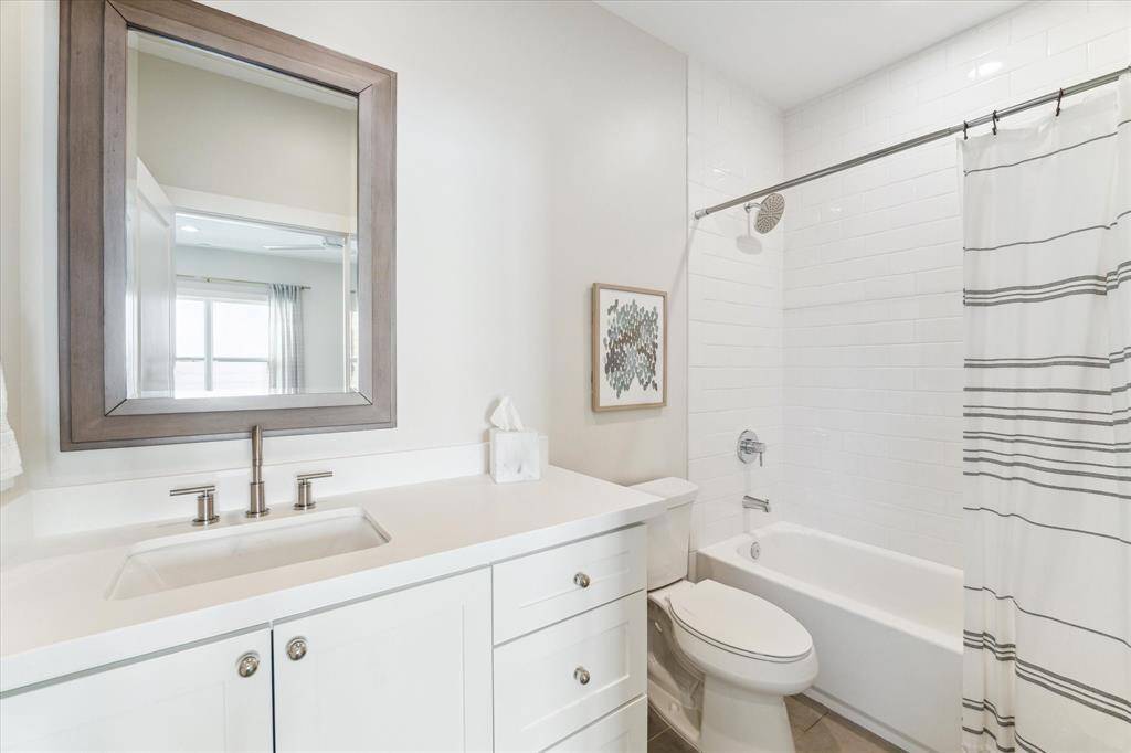 Located just off the upstairs flex space, this full bathroom features clean, modern finishes including white shaker cabinetry, brushed nickel fixtures, and a sleek quartz countertop. A tiled tub/shower combo with classic white subway tile offers versatility for guests or daily use.