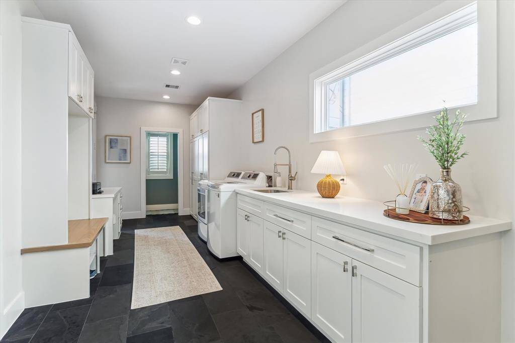 This multifunctional mudroom is both stylish and efficient, featuring built-in cabinetry, a drop zone with desk space, and a full-size laundry setup. A deep utility sink and overhead storage add convenience, while slate tile flooring ensures durability for everyday use.