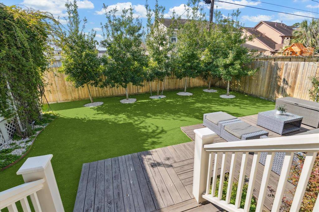 The backyard features a low-maintenance turf lawn surrounded by mature trees for added privacy and shade. A raised deck extends from the screened-in porch, offering a versatile space for outdoor lounging or entertaining in a lush, green setting.