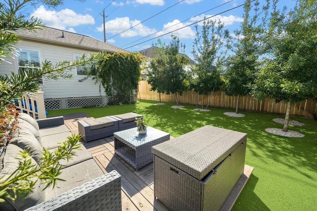 An alternate view of the backyard highlights the elevated deck and lush privacy landscaping. Low-maintenance turf keeps the space green year-round, while mature trees and climbing vines add a natural backdrop for outdoor relaxation or play.4o