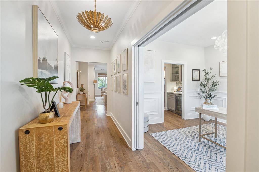Crisp white walls, curated artwork, and warm wood flooring make this entry hall feel bright and polished. A sculptural light fixture adds a touch of glamour, while the console table provides the perfect perch for statement décor.