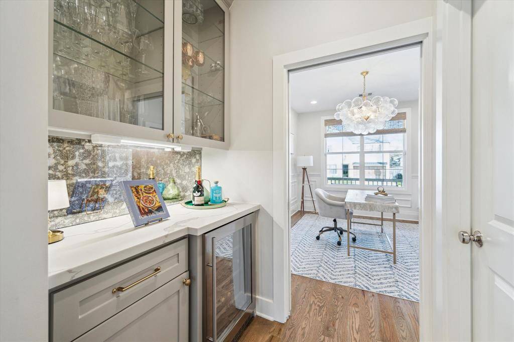 Tucked just off the front room, this stylish wet bar is outfitted with glass-front cabinetry, a wine fridge, and an eye-catching antique mirror backsplash—perfect for entertaining or adding a touch of luxury to your workday.