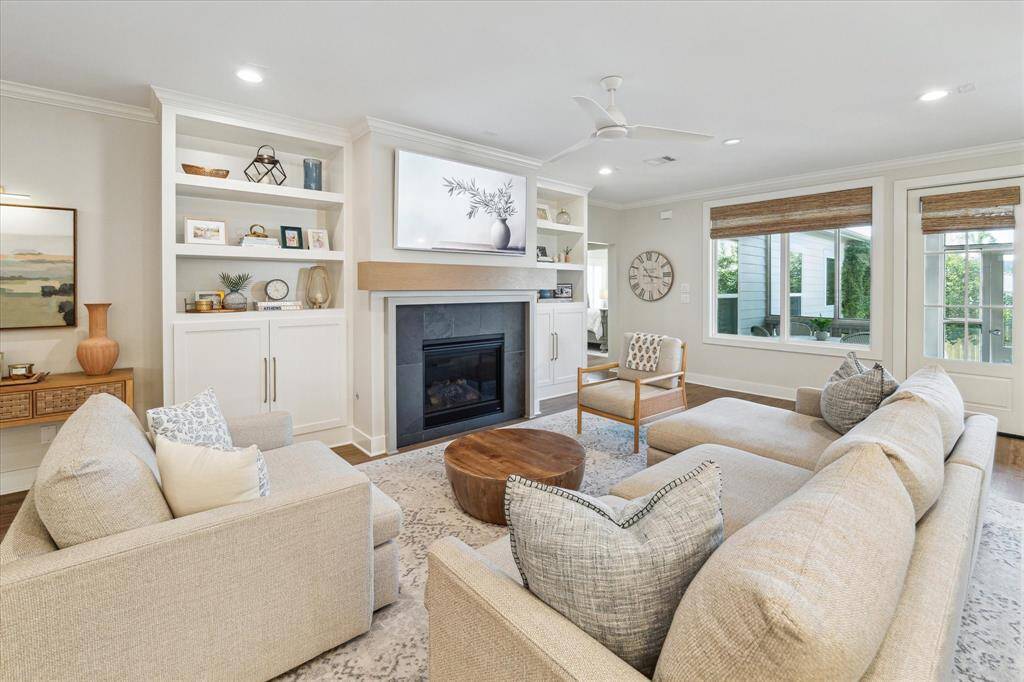 Large windows, built-in shelving, and a sleek gas fireplace define this open-concept living room. Neutral tones and layered textures create a warm, airy feel, while French doors connect seamlessly to the outdoor living area.
