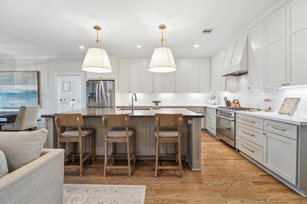 This thoughtfully designed kitchen combines refined aesthetics with practical function. Shaker-style cabinetry in a soft, neutral hue stretches to the ceiling, offering abundant storage and a seamless, built-in look. Sleek quartz countertops with subtle veining pair beautifully with the deep, contrasting island that doubles as a prep space and casual dining spot, complete with extra seating option.