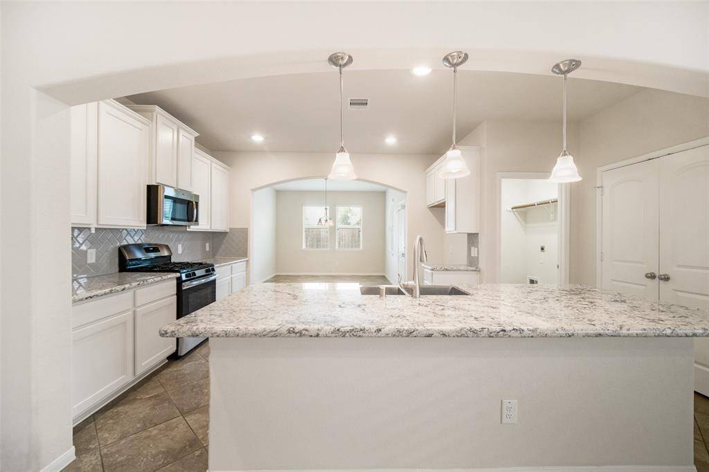 The kitchen features sleek granite countertops, an eat-at bar top with pendant lighting, recessed lights, a pantry, and tile flooring, combining both style and functionality.