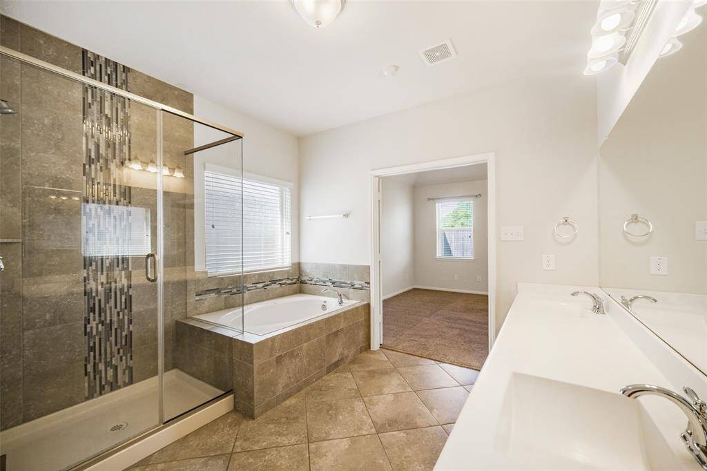 Tile flooring extends throughout the en-suite, complemented by stylish tile accents in the glass-enclosed shower and along the soaking tub for a cohesive look.