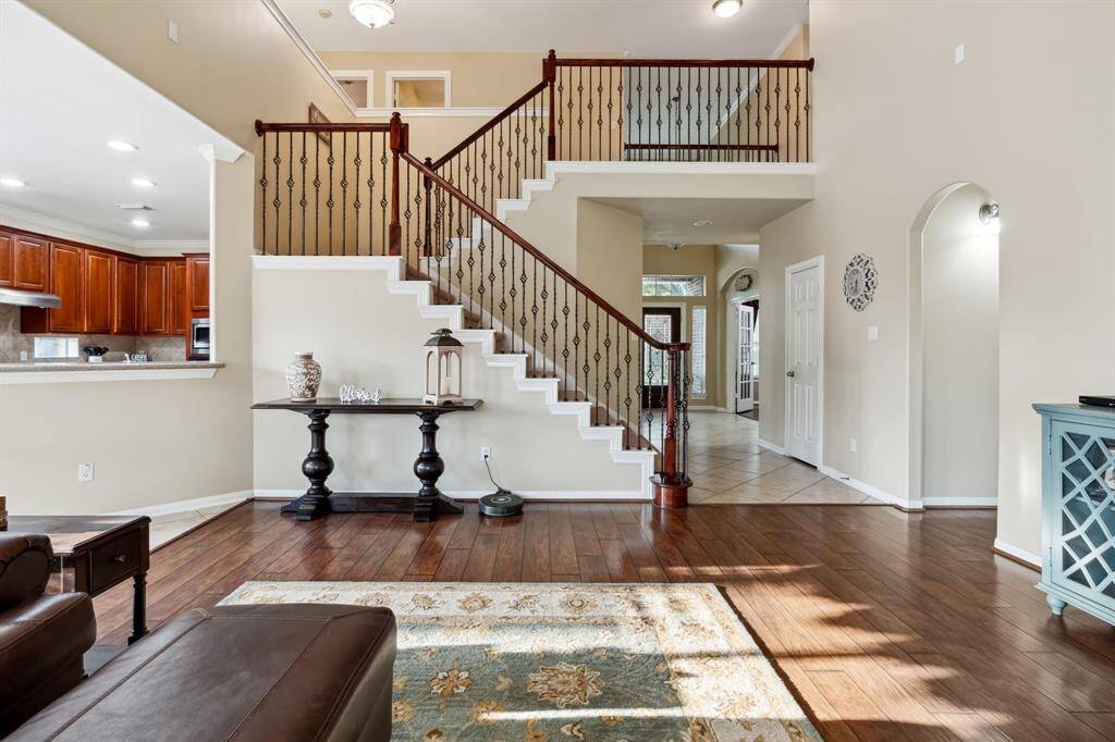 This spacious living area features elegant wood floors, a stylish staircase with wrought iron balusters, and an open view into the kitchen with rich wooden cabinetry.