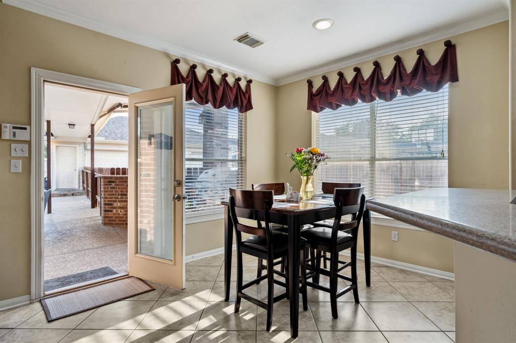 Bright breakfast nook with large windows, leading to the covered patio through a glass door. Features tiled flooring and a cozy dining setup.