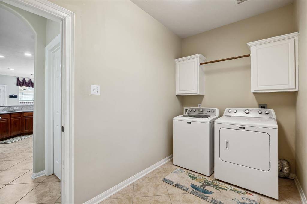 Laundry room with white cabinetry for storage, and a neutral color palette. The room is tiled and connects to the kitchen area.